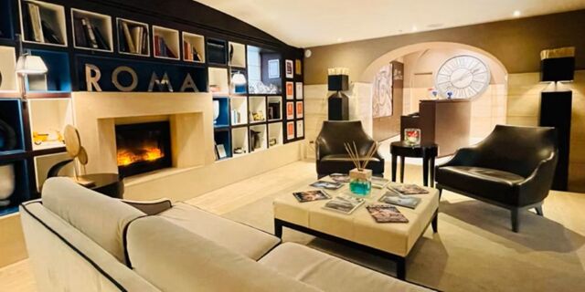 Modern lounge area at Hotel Indigo Rome-St.George featuring a beige sofa, two black armchairs, a coffee table, and a lit fireplace