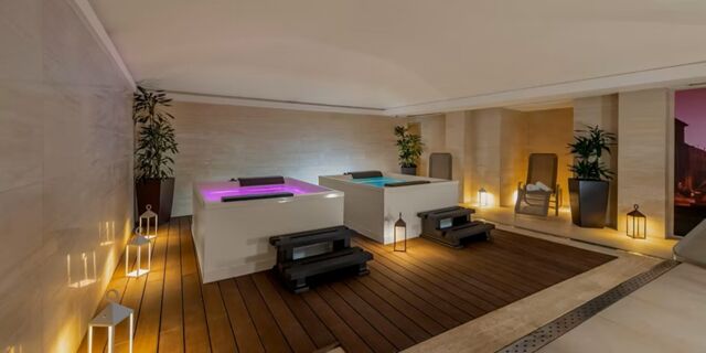 Two illuminated hot tubs with black steps on wooden flooring surrounded by plants and lanterns inside Hotel Indigo Rome-St.George spa area