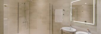 Bathroom interior at NH Collection Milano Porta Nuova featuring a glass shower, white towel on rack, illuminated mirror, and double sink fixtures