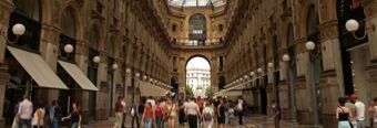 Crowd of people walking through a historic arched gallery with decorative lighting, featuring NH Collection Milano Porta Nuova nearby