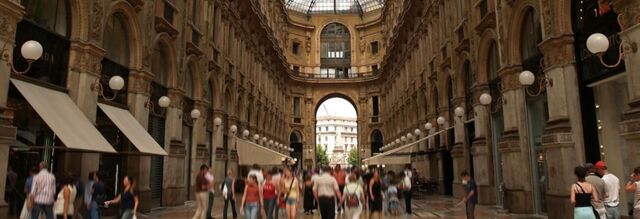 Crowd of people walking through a historic arched gallery with decorative lighting, featuring NH Collection Milano Porta Nuova nearby