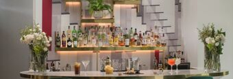 Bar counter with a variety of liquor bottles on illuminated shelves, cocktails, snacks, and floral arrangements at NH Collection Milano Porta Nuova
