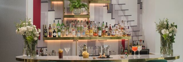 Bar counter with a variety of liquor bottles on illuminated shelves, cocktails, snacks, and floral arrangements at NH Collection Milano Porta Nuova