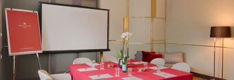 Meeting room with red tablecloth, white chairs, projector screen, flip chart, and lamp at NH Collection Milano Porta Nuova