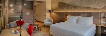Hotel room at NH Collection Milano Porta Nuova featuring a king bed with white linens, a gray sofa, armchair, desk, and wooden flooring