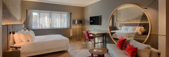 Spacious hotel room at NH Collection Milano Porta Nuova with a large bed, sofa with red cushions, round mirror, and desk area with chair