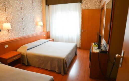 Hotel room at EcoHotel La Residenza with two beds, wooden flooring, bedside tables, lamp fixtures, TV, and a window with curtains