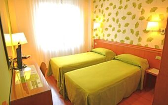 Twin beds with green covers in a room at EcoHotel La Residenza with wooden furniture, yellow walls, and natural light from a window
