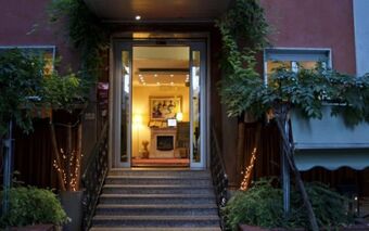 Entrance of EcoHotel La Residenza with stone stairs, black metal railings, and illuminated interior showing artwork and warm lighting