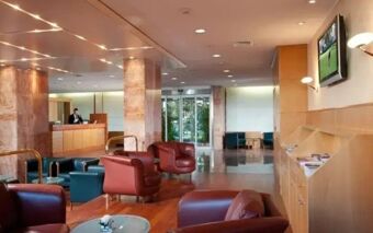 Hotel Raffaello lobby with leather armchairs, a reception desk, marble pillars, wooden flooring, and a wall-mounted television