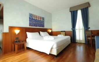 Spacious hotel room at Hotel Raffaello with two single beds, wooden flooring, wall lamps, a painting, and blue curtains on the window