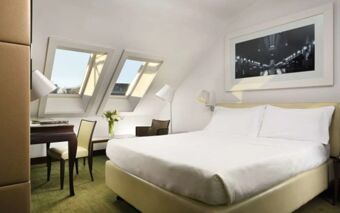 Bright hotel room at Hotel Una Cusani featuring a large bed with white linens, desk, chairs, and two skylight windows