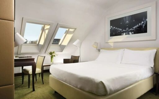 Bright hotel room at Hotel Una Cusani featuring a large bed with white linens, desk, chairs, and two skylight windows