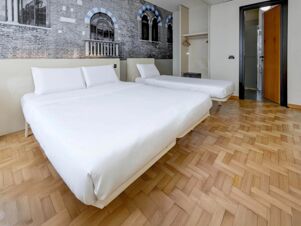 Two neatly made beds with white linens in a hotel room featuring a brick wall mural and wooden parquet floor at B&B Hotel Verona