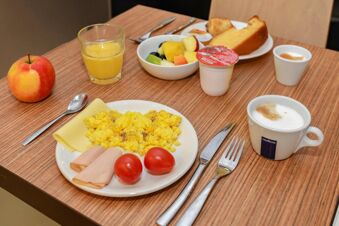 Breakfast spread with scrambled eggs, cherry tomatoes, rolled ham, cheese, fruit salad, orange juice, coffee, and bread at B&B Hotel Verona