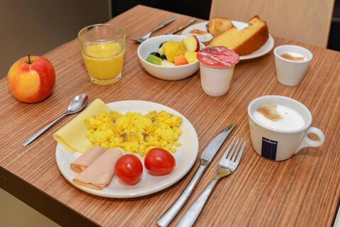Breakfast spread with scrambled eggs, cherry tomatoes, rolled ham, cheese, fruit salad, orange juice, coffee, and bread at B&B Hotel Verona