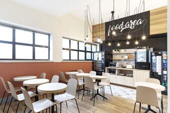Dining area with round tables and chairs, vending machines, microwaves, toaster, and hanging lights at B&B Hotel Verona