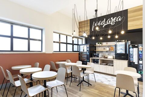 Dining area with round tables and chairs, vending machines, microwaves, toaster, and hanging lights at B&B Hotel Verona