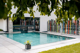 Outdoor pool with clear water next to a white building with a ski rack of colorful skis at Hotel Wochtla Buam