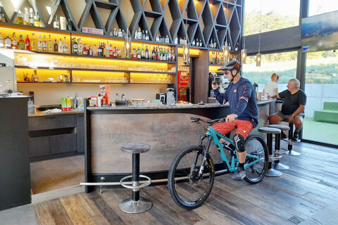 A man with a mountain bike wearing a helmet inside a bar area with bottles and glasses at Hotel Wochtla Buam