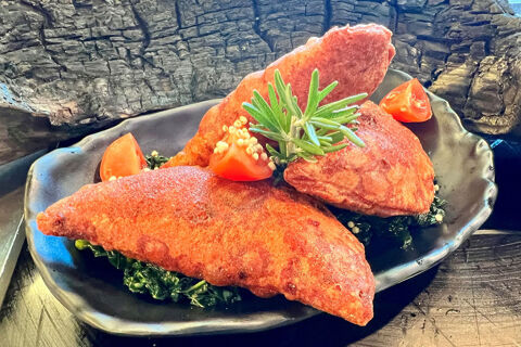Two pieces of fried meat with green garnish and tomato wedges on a black plate at Hotel Wochtla Buam