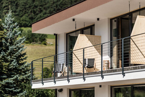 Balcony with black railing, wooden privacy walls, two black and white striped chairs, and tree logs at Hotel Wochtla Buam