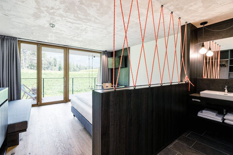 Modern hotel room at Hotel Wochtla Buam with a bed, wood flooring, large sliding glass doors, and a mounted TV visible