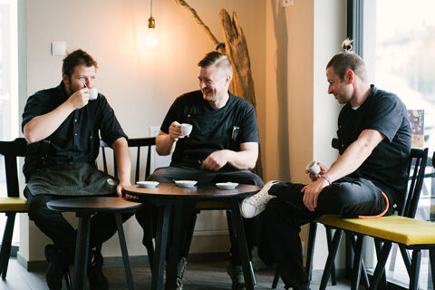 Three men dressed in black uniforms sit around a small table drinking coffee inside Hotel Wochtla Buam