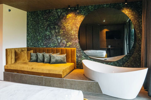 Hotel Wochtla Buam room featuring a mustard yellow couch with pillows, a white freestanding bathtub, and a large round mirror