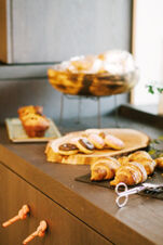 A selection of croissants, frosted donuts, muffins, and bread on wooden and metal trays at Hotel Wochtla Buam