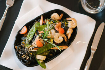 A black dish with shrimp, snow peas, cherry tomatoes, black pasta, and a sprig of rosemary served at Hotel Wochtla Buam
