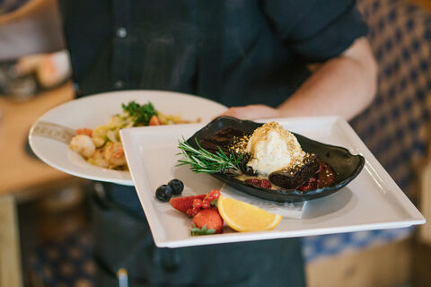 A server holding two plates with a chocolate dessert topped with ice cream and fruit served on a white tray at Hotel Wochtla Buam