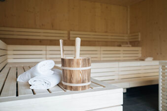Wooden bucket with ladles and two folded white towels on a wooden bench inside a sauna at Hotel Wochtla Buam