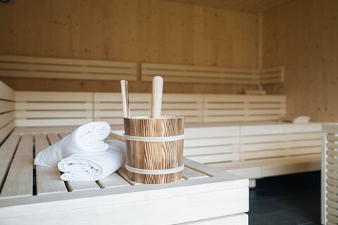 Wooden bucket with ladles and two folded white towels on a wooden bench inside a sauna at Hotel Wochtla Buam