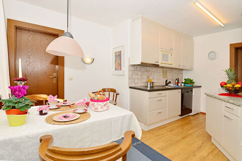 Kitchen and dining area with white cabinets, wooden chairs, fruit bowl, and table set for breakfast at Ferienwohnungen W&ouml;rz