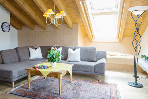 Living area with gray sectional sofa, wooden table with plant, floor lamp, and skylight at Ferienwohnungen W&ouml;rz