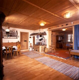 Spacious wooden interior of G&auml;stehaus zur F&auml;rbe Ferien-Appartements with dining area, rugs, wood ceiling, and kitchen with hanging pots and pans