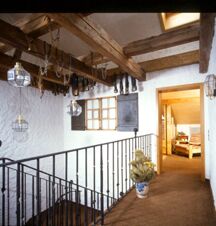 Indoor hallway with wooden ceiling beams, hanging lanterns, black iron railing, and open doorway at G&auml;stehaus zur F&auml;rbe Ferien-Appartements