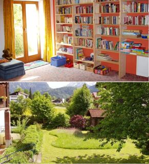 Ein gem&uuml;tlicher Leseraum mit B&uuml;cherregalen und Sitzecke sowie ein gr&uuml;ner Garten mit Bergblick im G&auml;stehaus zur F&auml;rbe Ferien-Appartements.