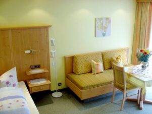 Room interior at G&auml;stehaus zur F&auml;rbe Ferien-Appartements with a bed, wooden sofa with cushions, small table, chair, and floral decorations