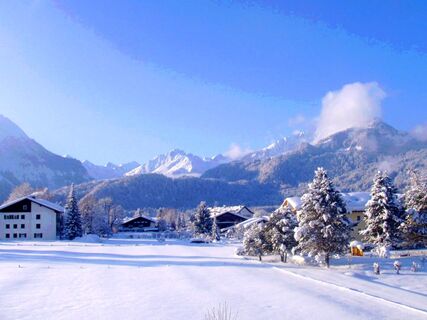 Winterliche Landschaft mit schneebedeckten B&auml;umen und H&auml;usern in den Bergen, G&auml;stehaus zur F&auml;rbe Ferien-Appartements im Hintergrund.