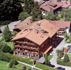 Large multi-story wooden building with balconies and flower boxes surrounded by trees and parked cars at G&auml;stehaus zur F&auml;rbe Ferien-Appartements
