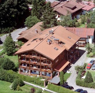 Large multi-story wooden building with balconies and flower boxes surrounded by trees and parked cars at G&auml;stehaus zur F&auml;rbe Ferien-Appartements