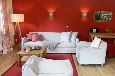 Living room in Landhaus Berktold with light gray sofa and armchair, wooden coffee table, red wall and wooden floor