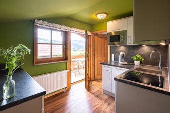 Kitchen room with green walls, wooden floor, white cabinets, a stove, coffee maker, and an open door to a balcony at Landhaus Berktold