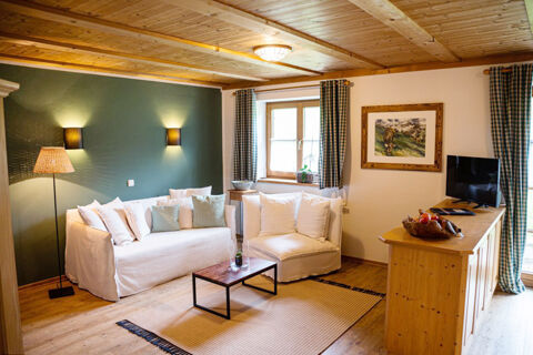 Cozy living room at Landhaus Berktold with white sofas, wooden ceiling and floor, green accent wall, and TV on wooden cabinet