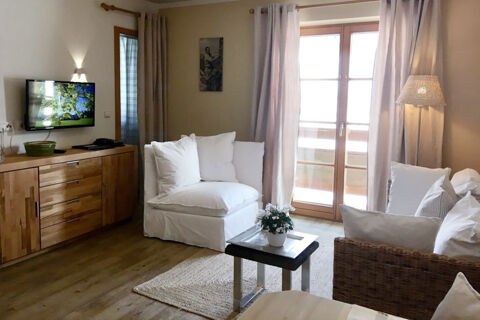 Living area at Landhaus Berktold with white cushioned chair and sofa, wooden cabinet, flat screen TV, and French doors with curtains