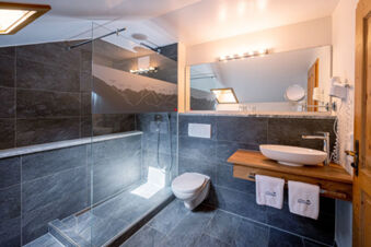 Modern bathroom with glass shower, wall-mounted toilet, wooden countertop with vessel sink, and towels in Landhaus Berktold