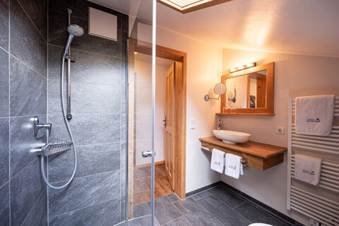 Modern bathroom in Landhaus Berktold with gray tiled shower, wooden vanity and mirror, and white towels on radiator and rack