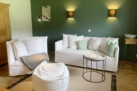 Living area at Landhaus Berktold with white couches, a matching ottoman, black metal round coffee table, and green wall lighting